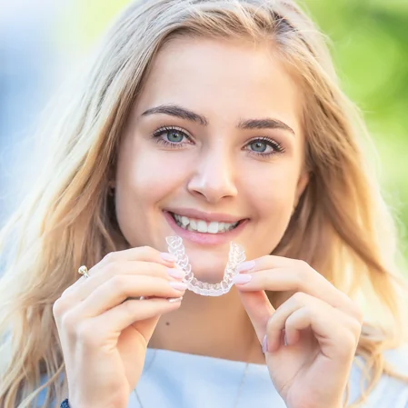 A young woman smiling and holding up her clear aligners